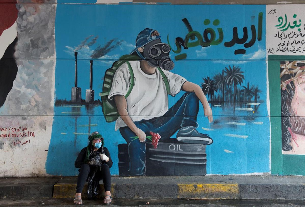 A protester rests by a mural with Arabic that reads, 'I want my oil,' in Baghdad in 2019.  THE ASSOCIATED PRESS